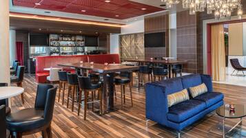 A modern bar area with a red ceiling, multiple seating options including a blue sofa and bar stools, and a variety of bar stools.