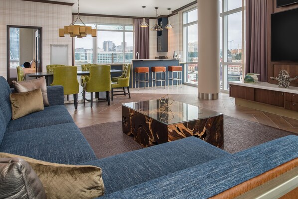Una sala de estar moderna con un sofá azul, una mesa de centro de vidrio y vistas a la ciudad a través de amplios ventanales.