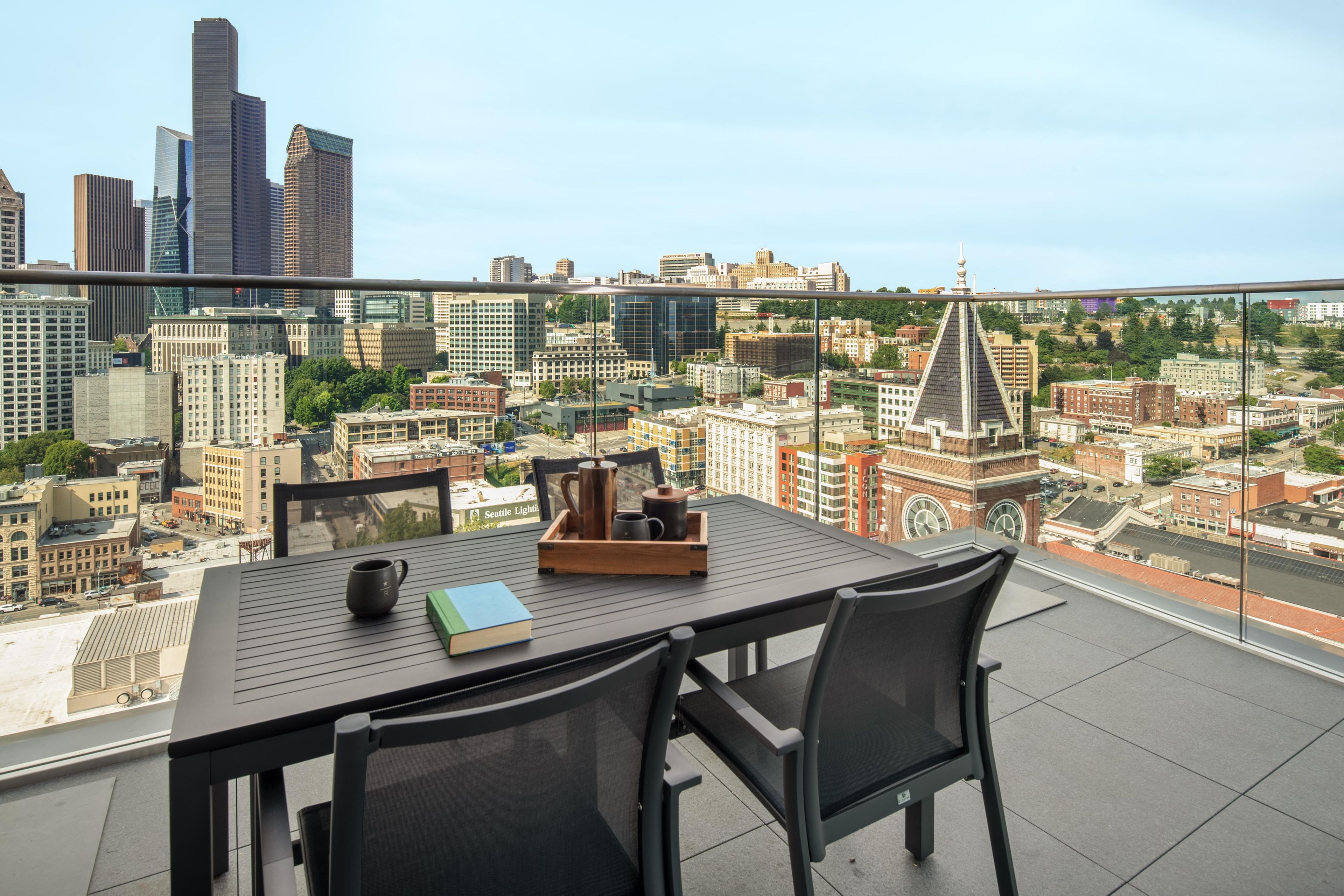 A balcony with a table, chairs, and a tray with a mug, book, and coffee pot.