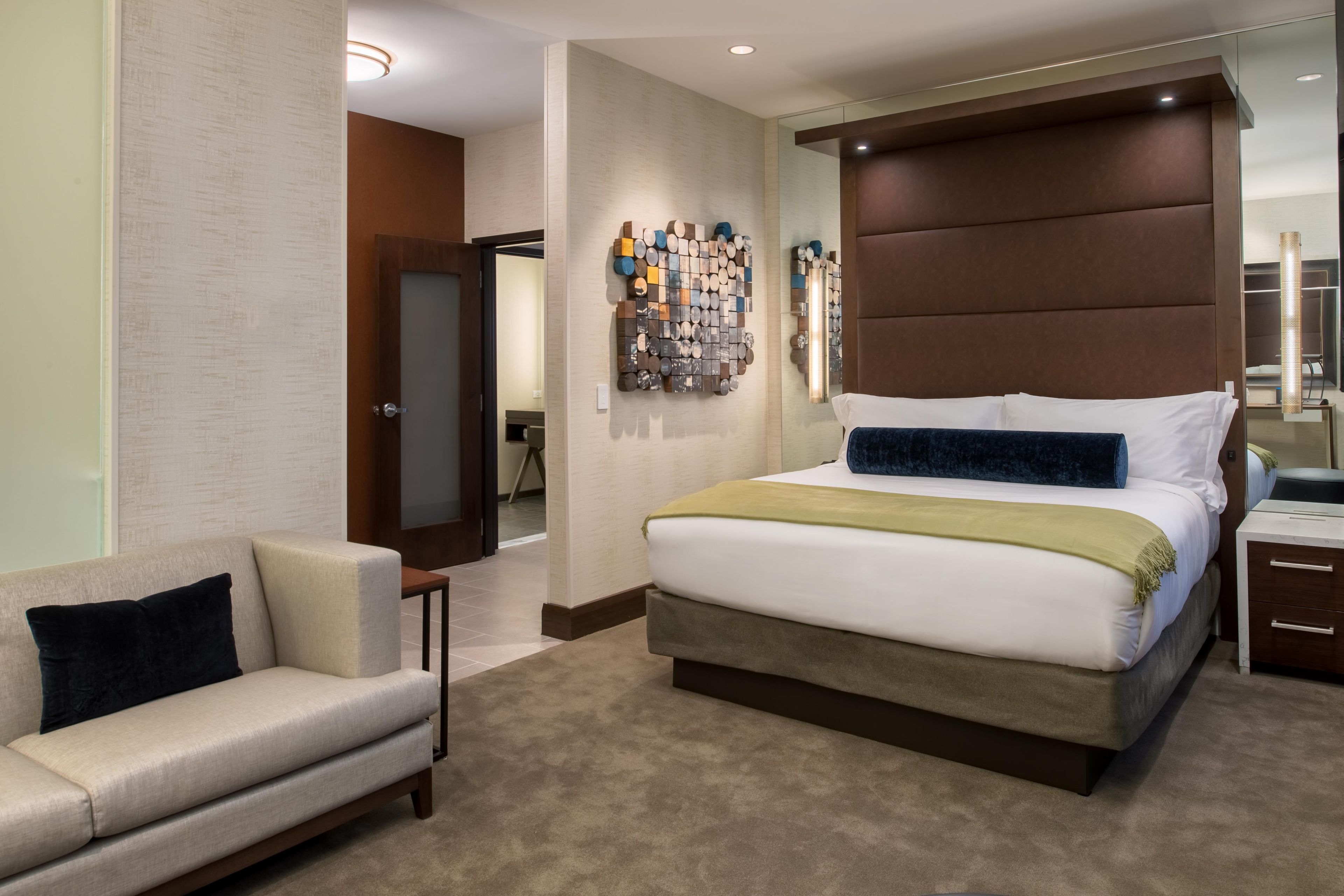 A hotel room with a bed, a sofa, a wall-mounted artwork, and a mirror.