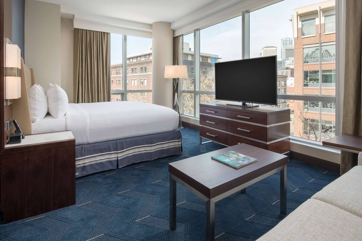 A hotel room with a bed, a desk, a TV, and a view of the city.