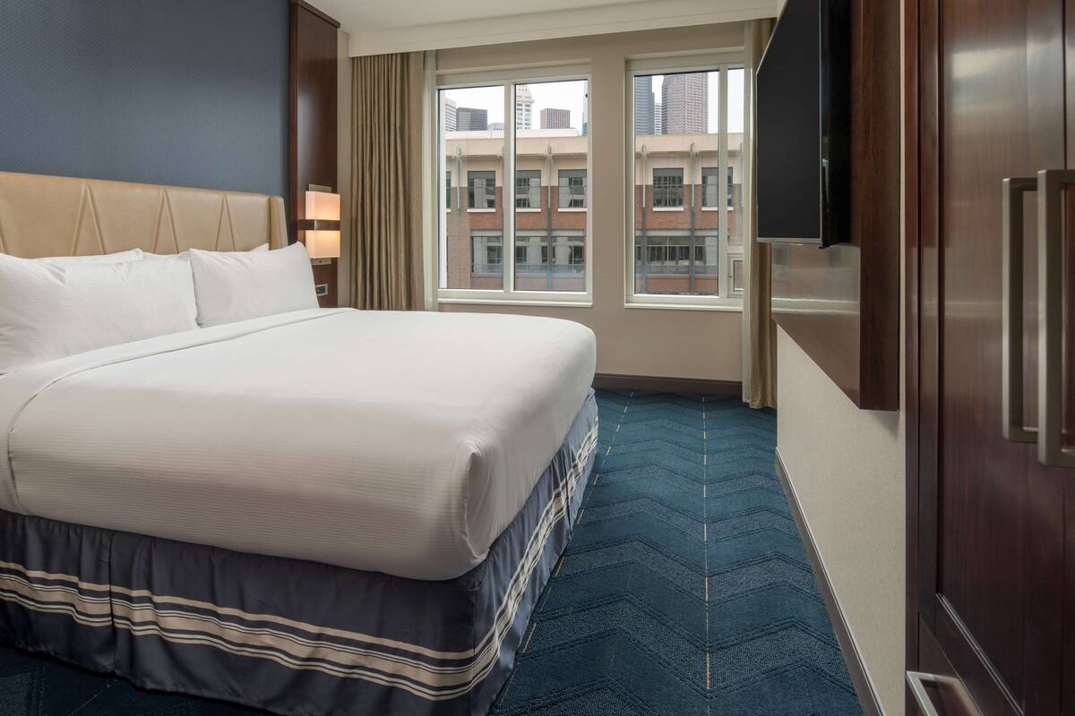 A hotel room with a large bed, a TV, and a window with a city view.