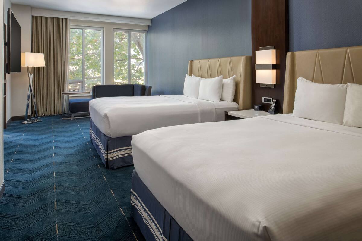 A hotel room with two beds, a desk, a chair, a TV, and a window with curtains.