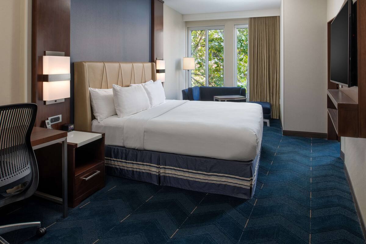A hotel room with a large bed, a desk with a chair, a television, and a window with curtains.