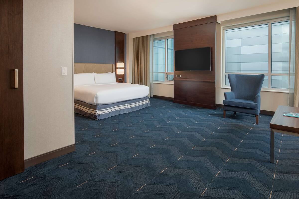 A hotel room with a bed, a TV, a chair, and a desk.