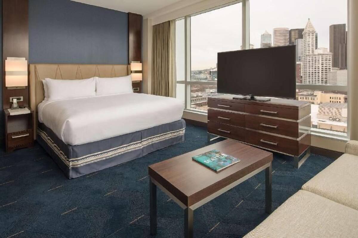 A hotel room with a large bed, a TV, a dresser, and a view of the city skyline.