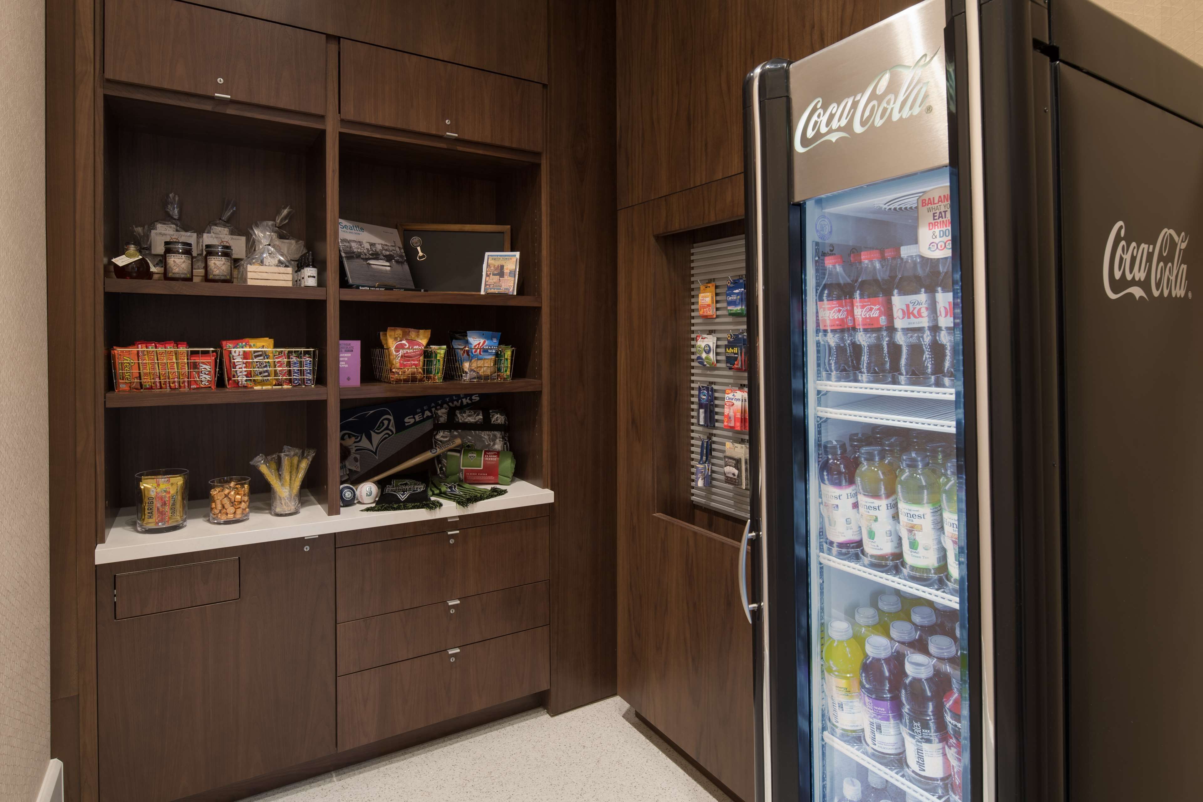 Una cocina con un refrigerador lleno de bebidas, un armario con bocadillos y una cafetera.