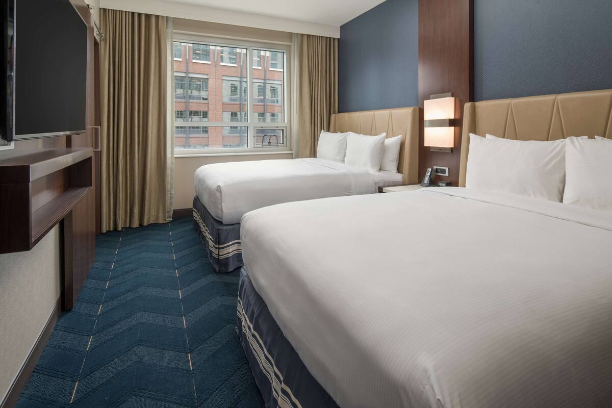 A hotel room with two beds, a TV, and a window with curtains.