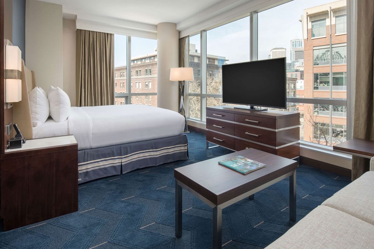 A hotel room with a bed, a TV, a desk, and a view of the city.