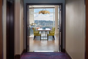 A view from a hallway to a dining area with a table and chairs, a hanging light fixture, and a cityscape view through a large window.