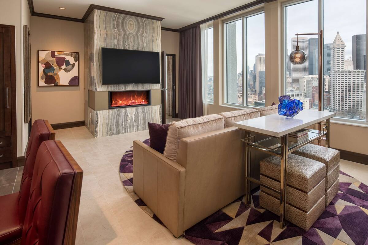 A modern living room with a fireplace, a sofa, a dining table, and a city view.