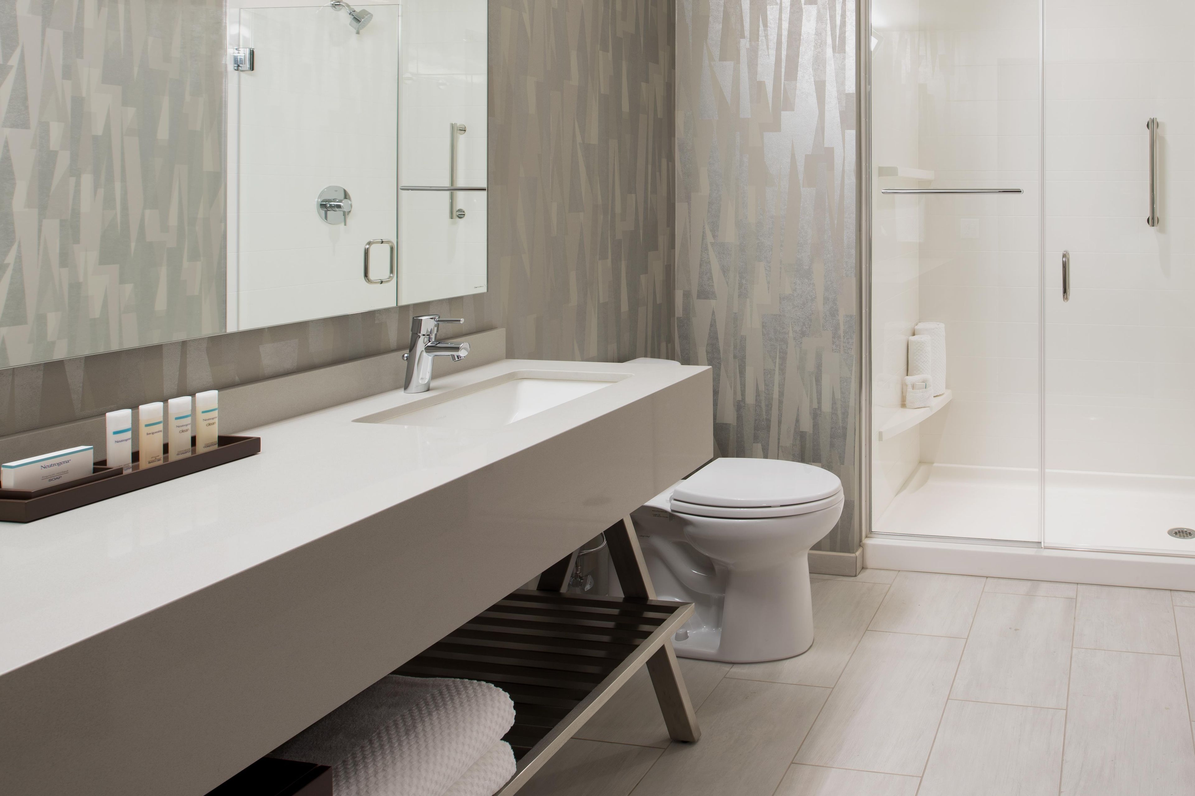 Une salle de bain moderne avec un grand miroir, un lavabo blanc, des toilettes et une douche séparée par une paroi de verre.