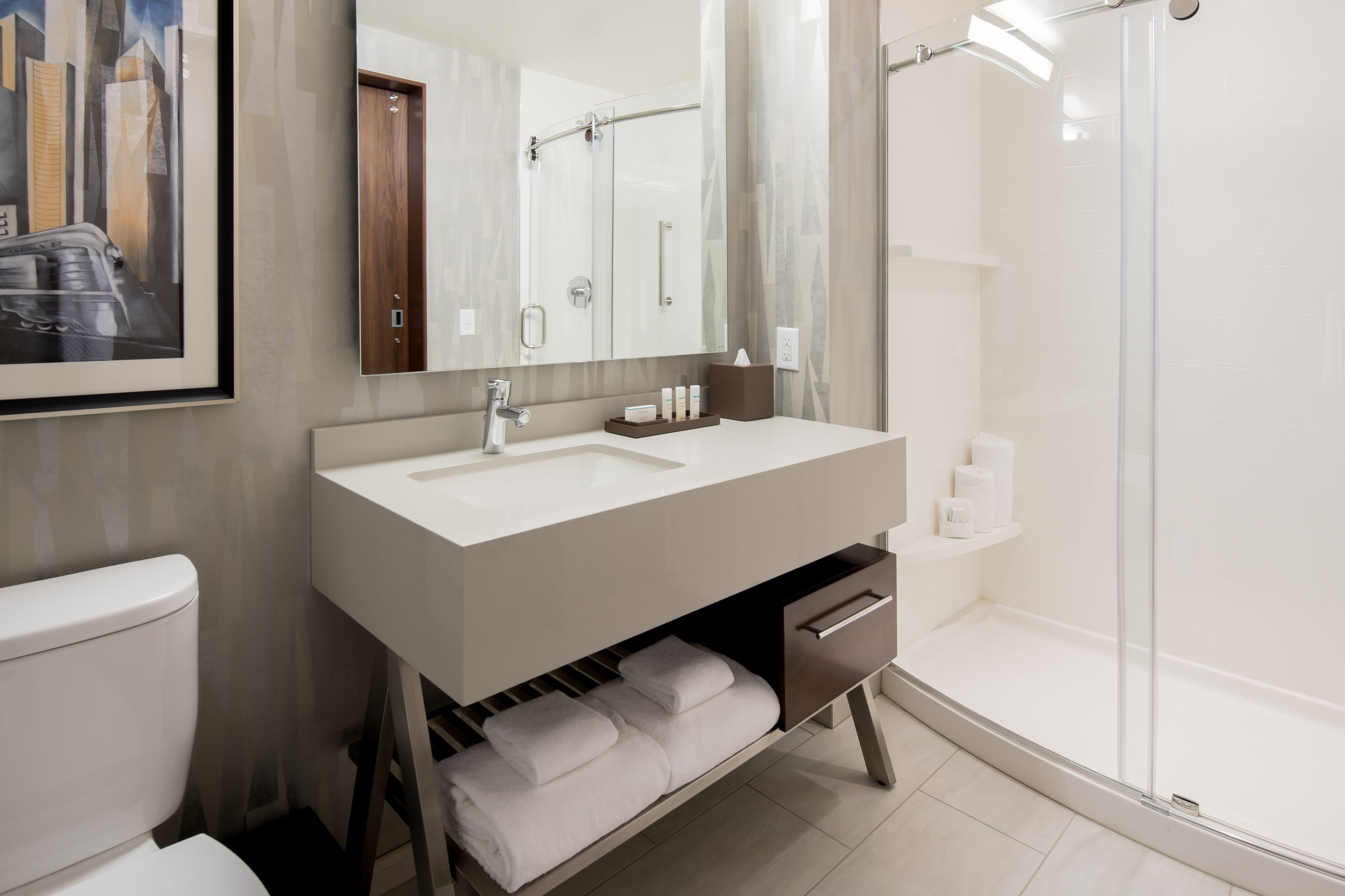 A modern bathroom with a white sink, a mirror, a shower, and a toilet.