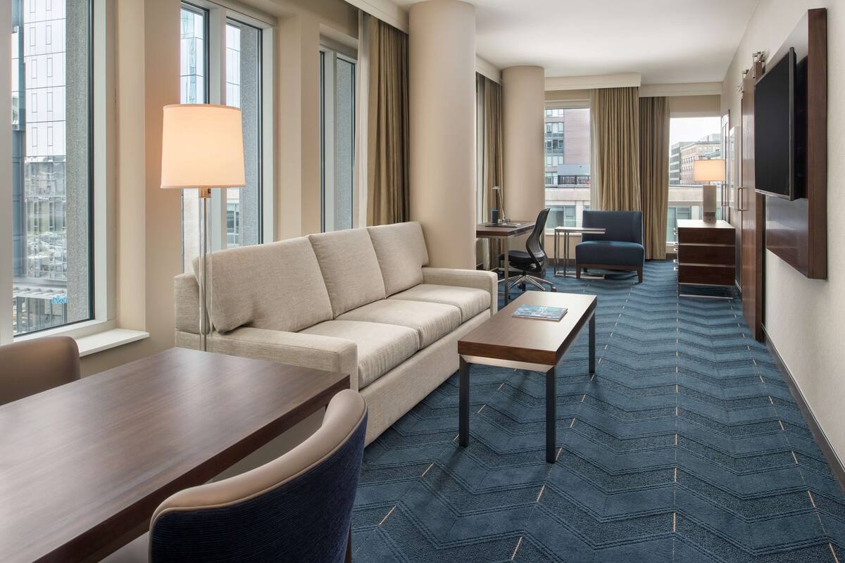 A hotel room with a sofa, a dining table, a coffee table, and a TV mounted on the wall.