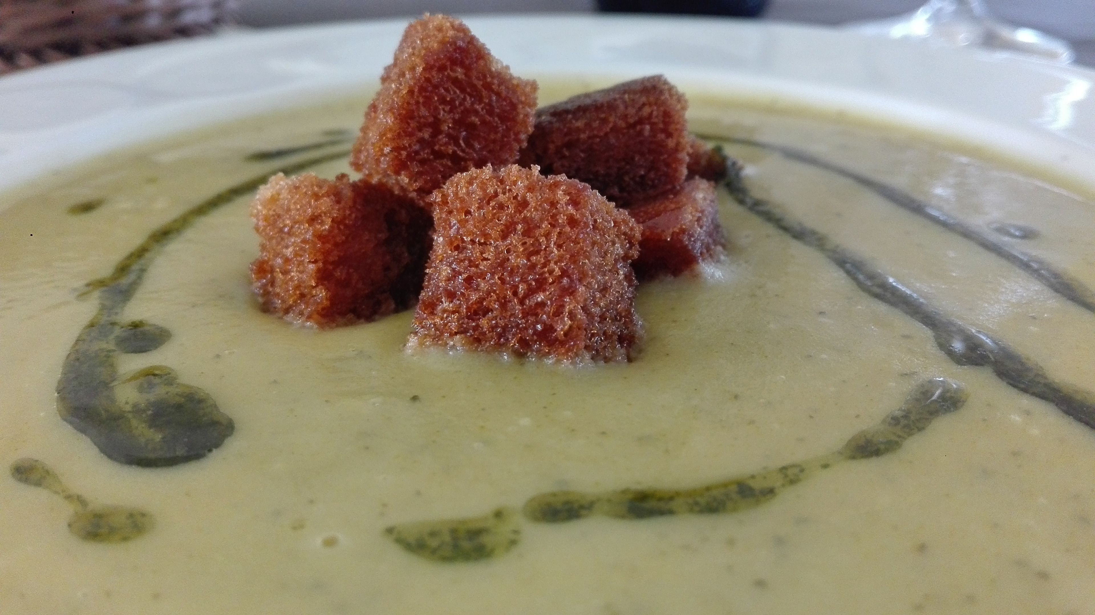 Un tazón de sopa con croutons y un chorrito de salsa verde.