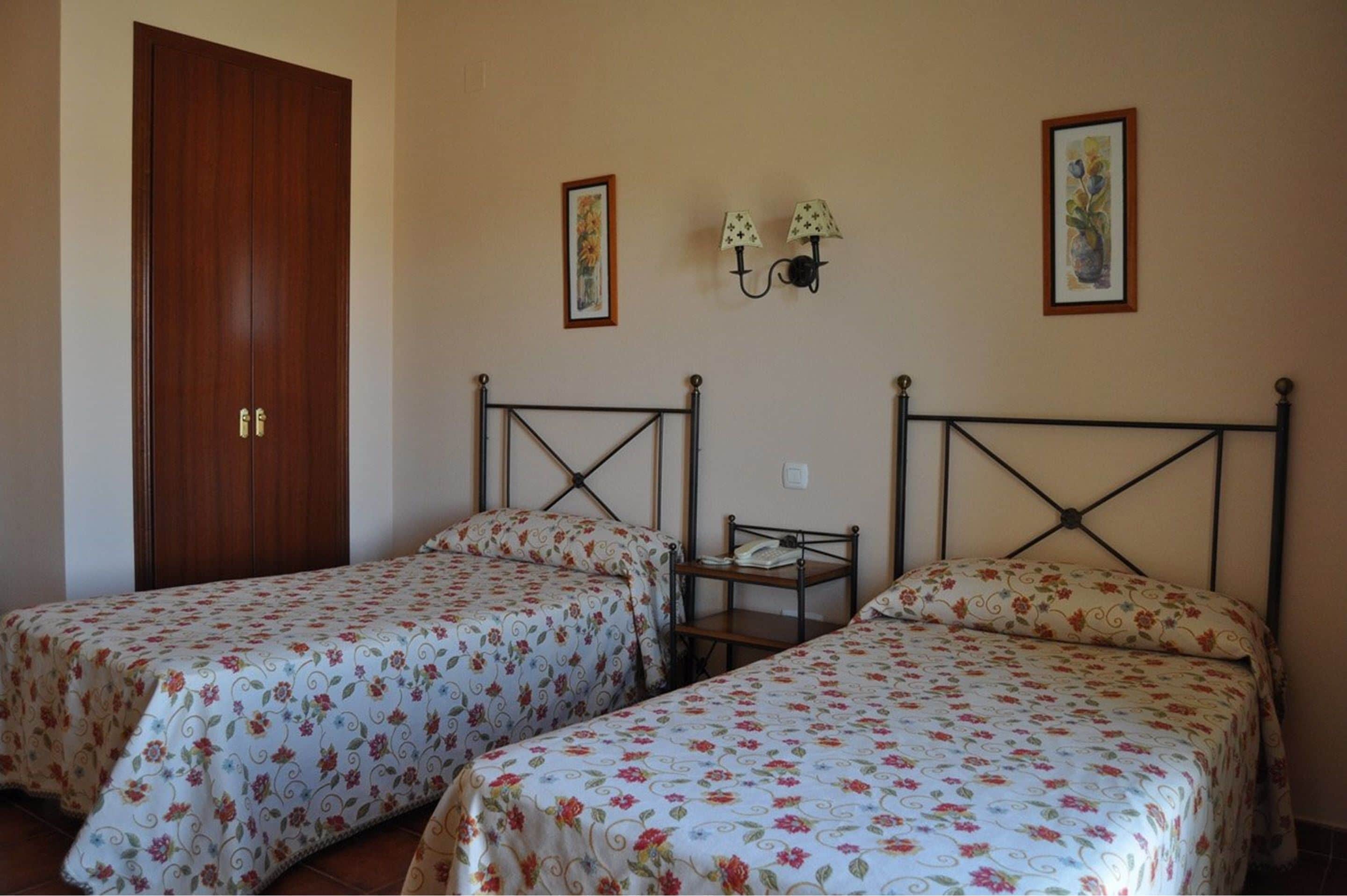 A bedroom with two single beds, a wooden door, and wall-mounted lamps.