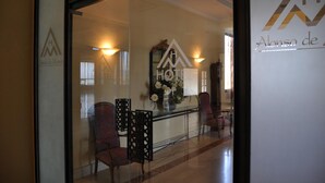 Zona de recepción de un hotel con un separador de vidrio, un mostrador de recepción y un cartel fijado a la pared.
