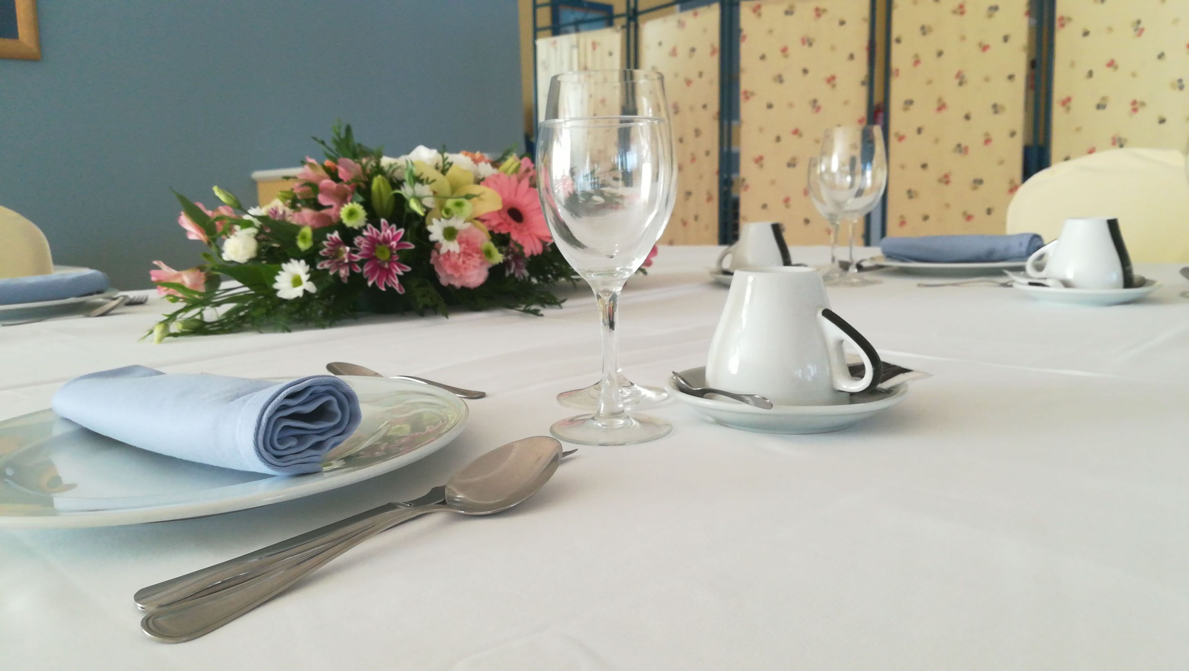 Une table à manger élégamment dressée, avec une serviette pliée, un verre, une tasse à thé et un centre de table floral.