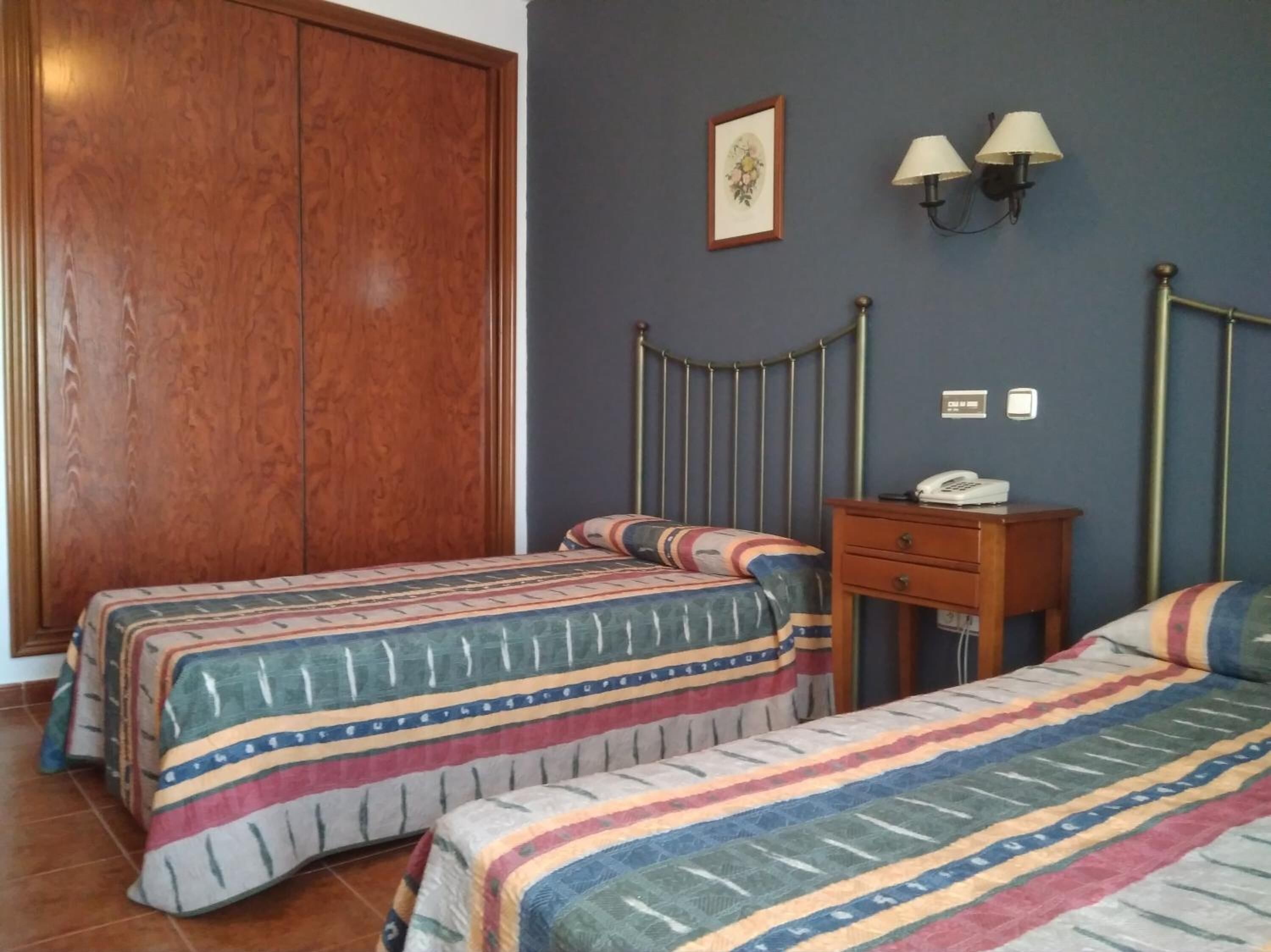 Een slaapkamer met twee bedden, een houten garderobe, een nachtkastje met een lamp en een ingelijste foto aan de muur.