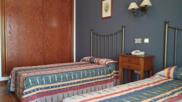 Een slaapkamer met twee bedden, een houten garderobe, een nachtkastje met een lamp en een ingelijste foto aan de muur.