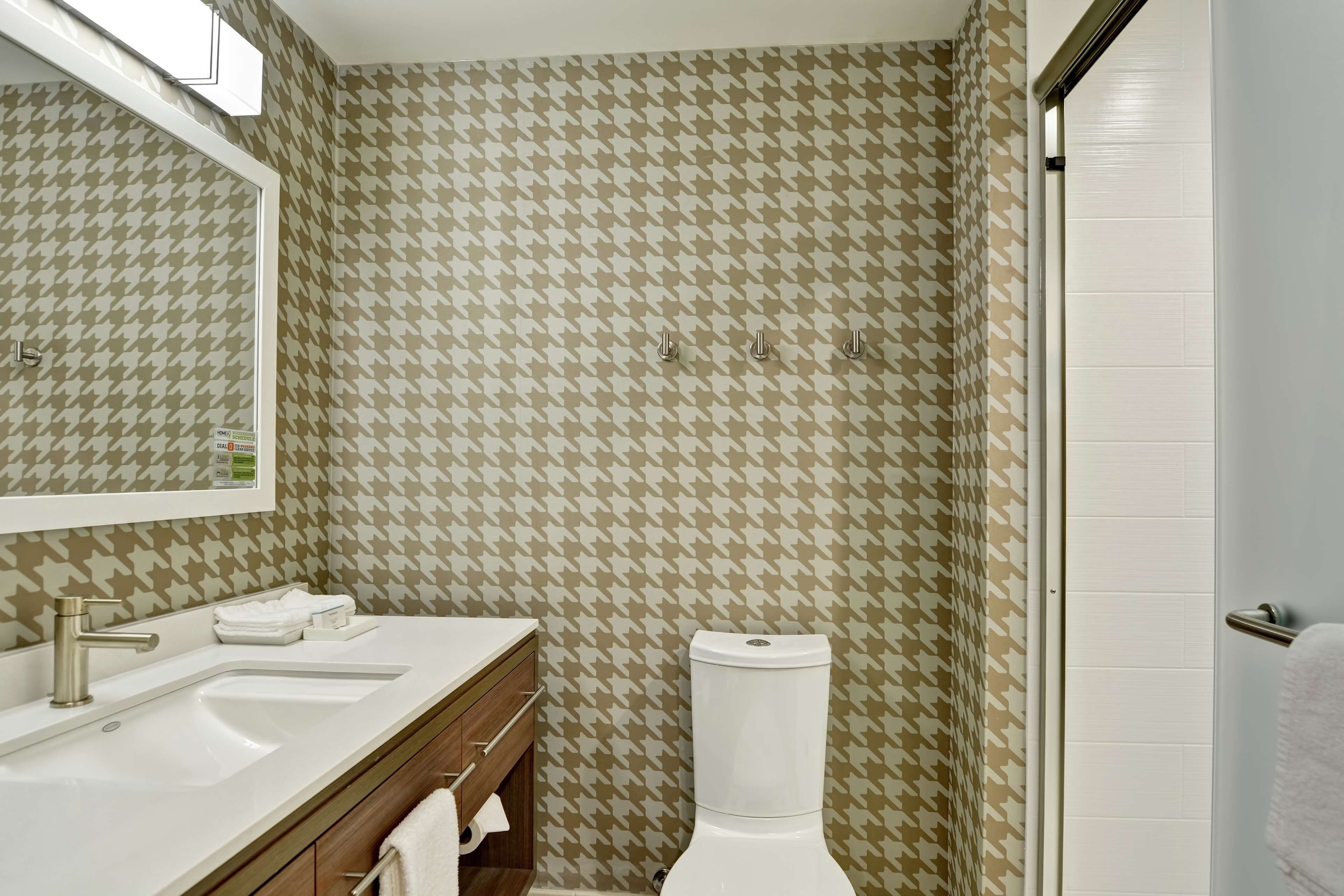A bathroom with a houndstooth patterned wall, a white sink with a mirror above it, and a toilet.