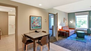 A modern hotel room with a dining area, a sofa, and a large window.