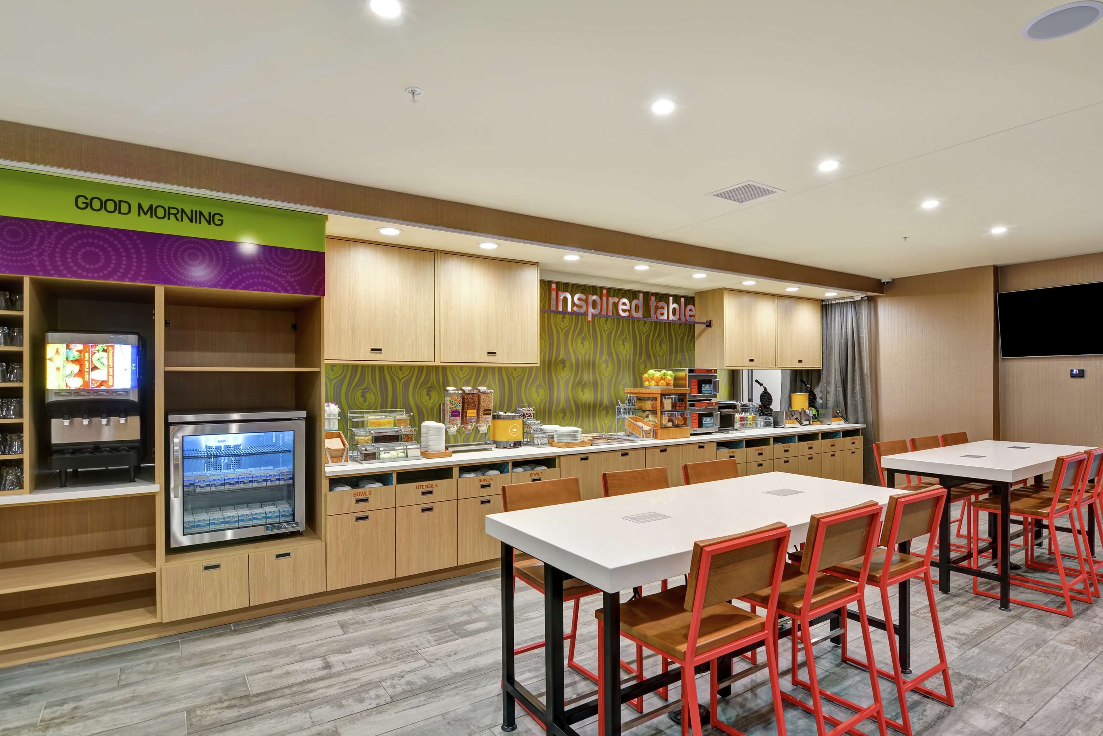A modern restaurant with a breakfast bar, seating area, and a counter with various food items.
