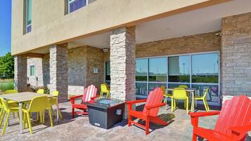 An outdoor patio area with stone pillars, yellow and red Adirondack chairs, and a glass-top table.
