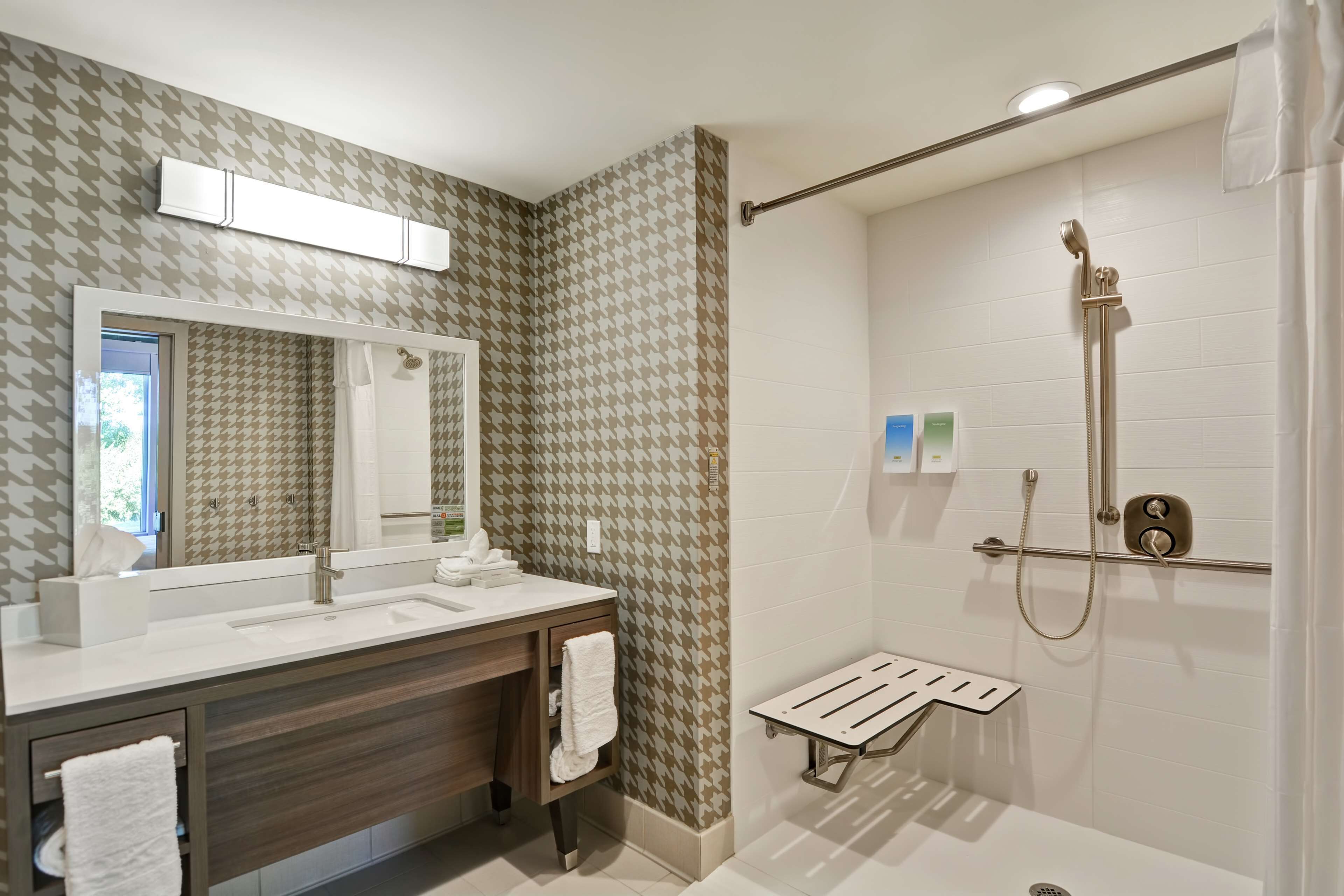 A modern bathroom with a large mirror, dual sinks, a shower with a handheld showerhead, and a towel rack.