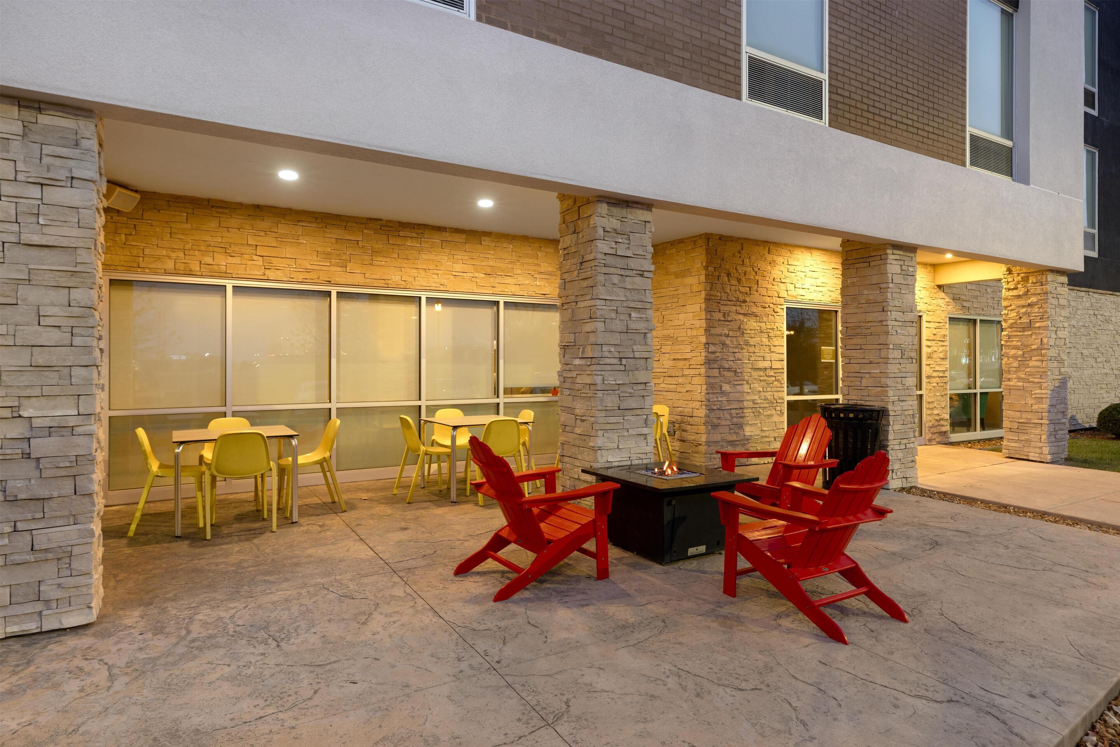 An outdoor patio with red and yellow chairs, a table, and stone pillars.