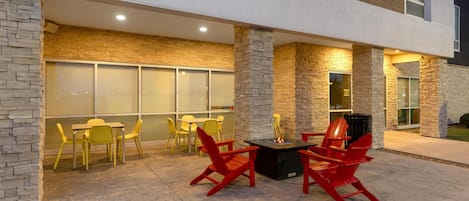 An outdoor patio with red and yellow chairs, a table, and stone pillars.