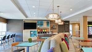 A modern cafe with a central seating area, a counter, and a kitchen visible in the background.