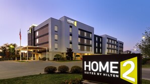 A modern hotel with a sign reading 'HOME 2 SUITES BY HILTON' and a flag.