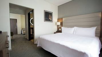 A hotel room with a large bed, a bedside table with a lamp, a door leading to a bathroom, and a framed picture on the wall.