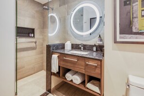 A modern bathroom with a glass-enclosed shower, a vanity with a marble countertop, and two large mirrors with illuminated frames. - Fiesta Inn Suites Aeropuerto del Bajío (Silao)