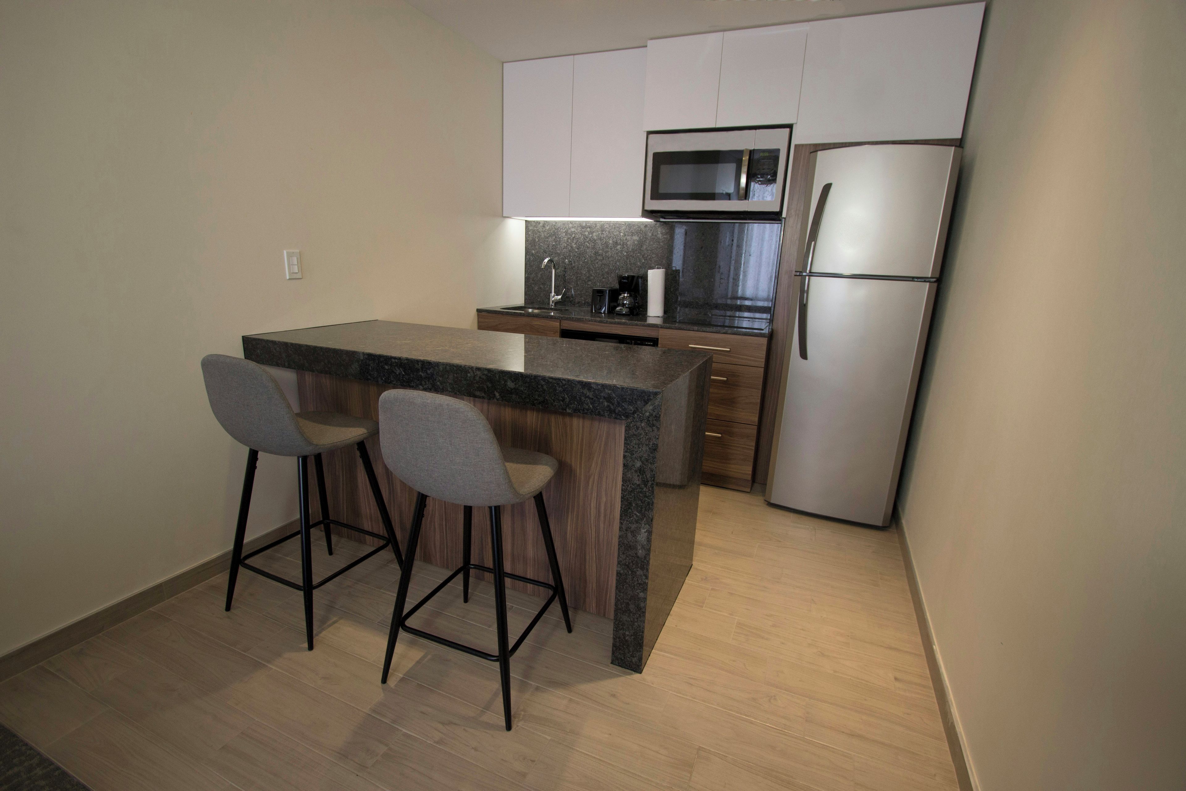 A modern kitchen with a central island, two bar stools, a microwave, and a refrigerator.