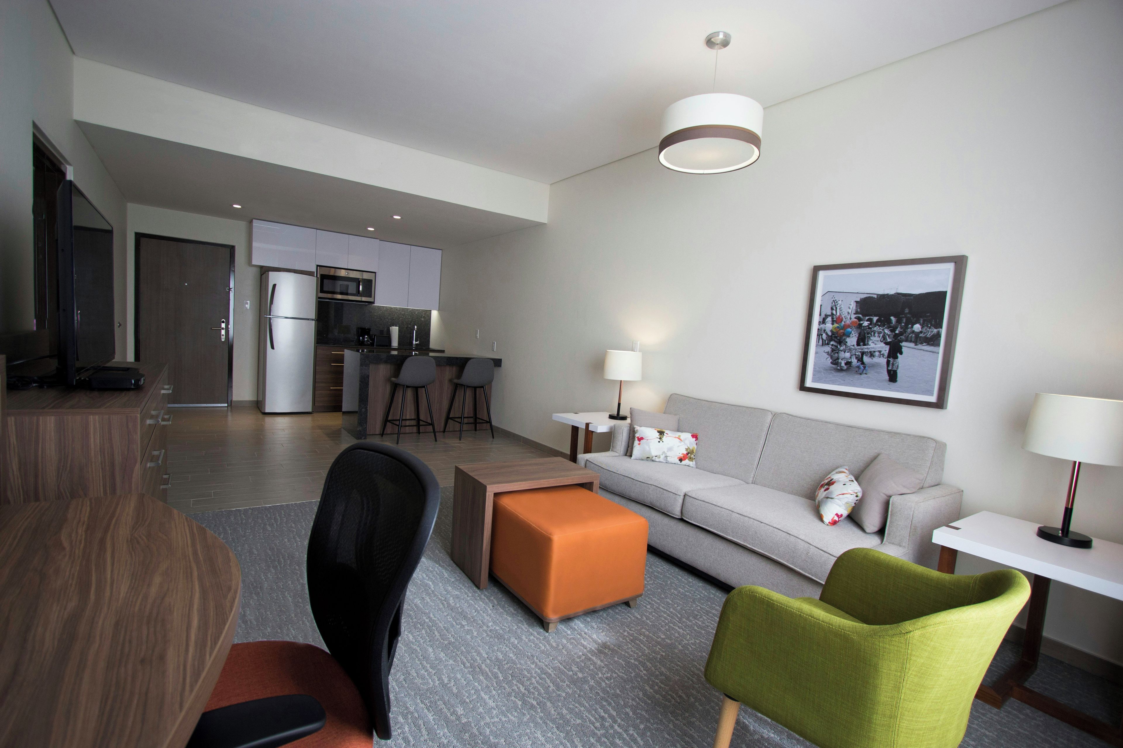 Una sala de estar moderna con sofá, otomanas y sillas, un comedor con mesa, y una cocina con refrigerador y microondas.
