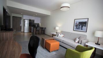 Una sala de estar moderna con sofá, otomanas y sillas, un comedor con mesa, y una cocina con refrigerador y microondas.