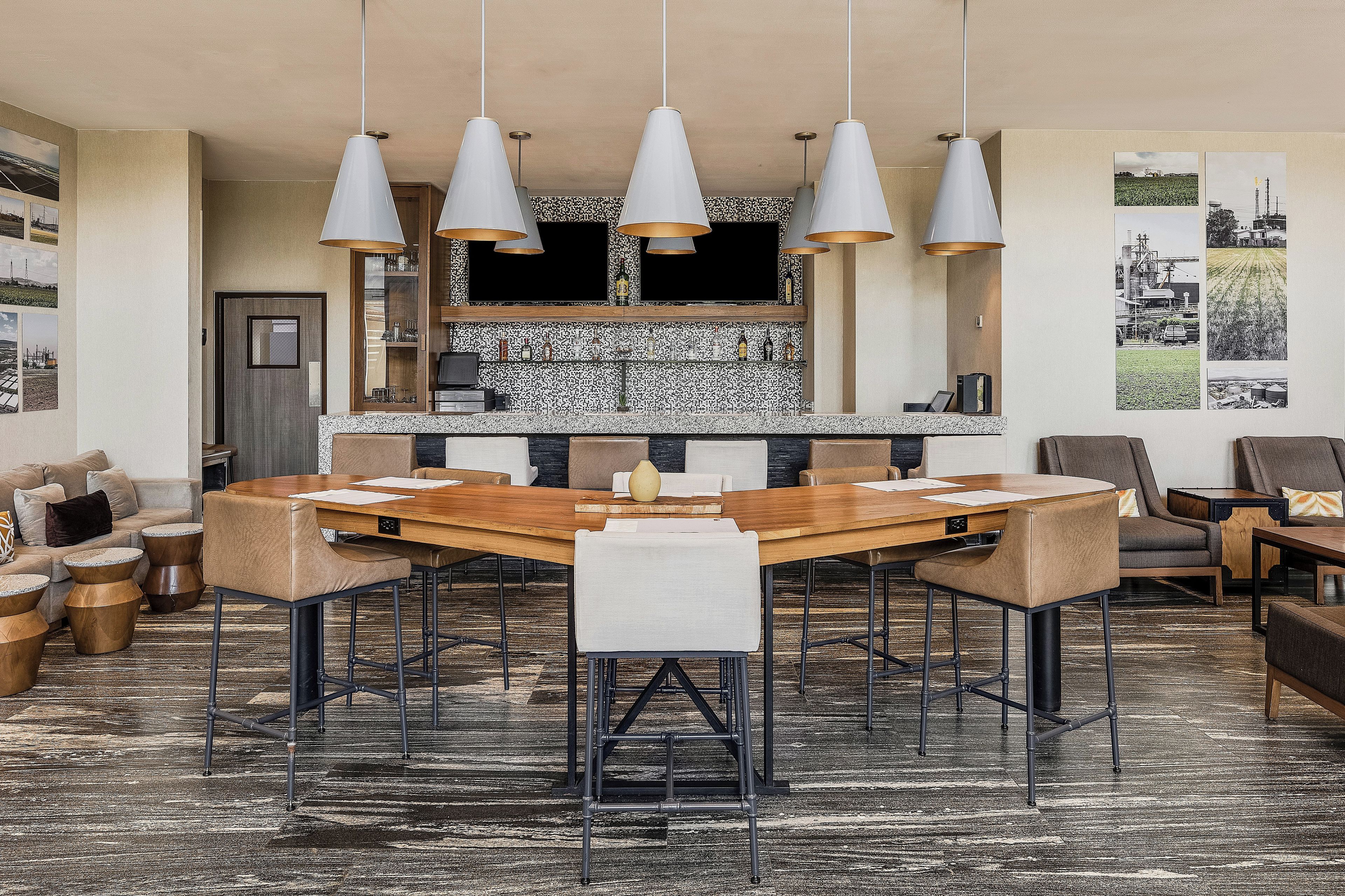 Un comedor moderno con una mesa y sillas de madera, iluminación colgante y una cocina al fondo.