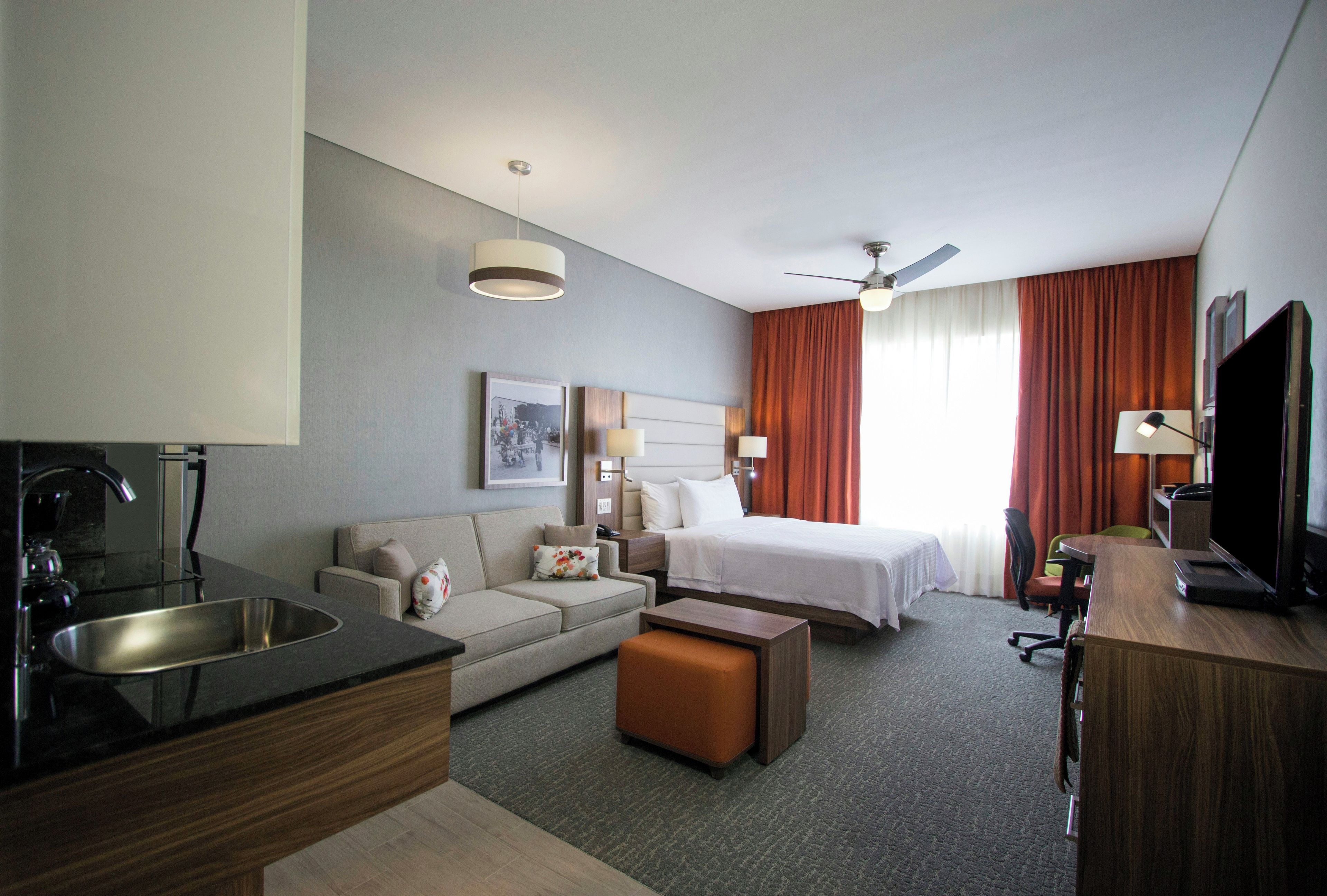 A hotel room with a bed, a sofa, a desk with a computer, a television, and a bathroom area.