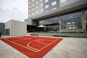 An outdoor basketball court adjacent to a modern building with large windows and a covered seating area.