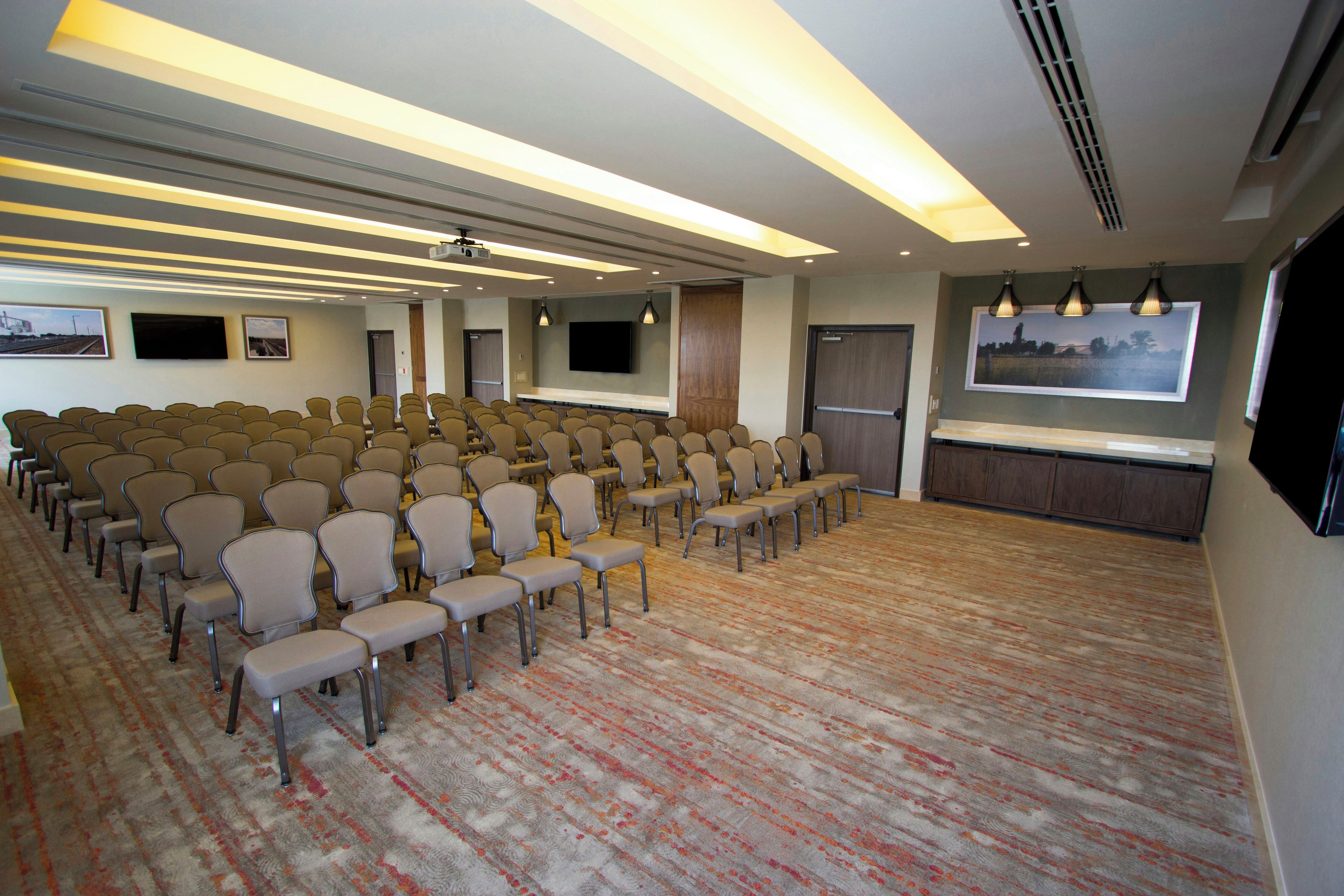 A conference room with rows of chairs, a large screen, and a projector.