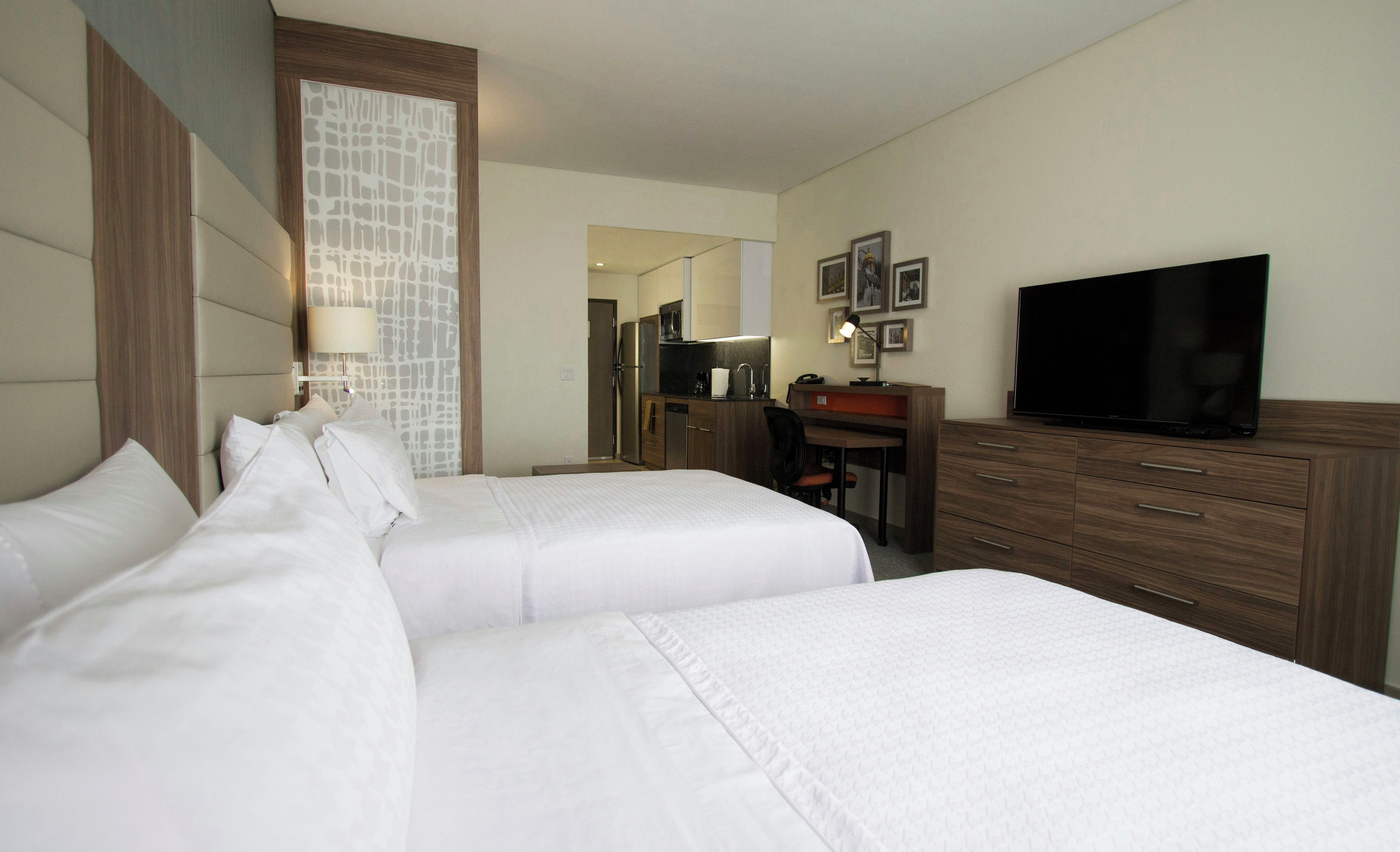 A hotel room with two beds, a desk, a television, and a kitchenette.