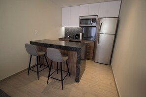 A modern kitchen with a granite countertop, stainless steel appliances, and two bar stools. - Fiesta Inn Suites Aeropuerto del Bajío (Silao)