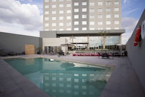 A hotel pool area with a clear view of the building, outdoor seating, and a lifebuoy on the wall. - Fiesta Inn Suites Aeropuerto del Bajío (Silao)