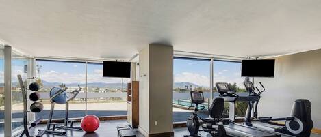 Un gimnasio con equipamiento de ejercicio, amplias ventanas y vistas al exterior.