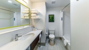 A modern bathroom with a white sink, mirror, and toilet. There are towels on a rack and a shower curtain.