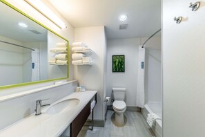 A modern bathroom with a white sink, mirror, and toilet. There are towels on a rack and a shower curtain.