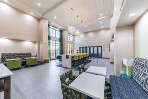 A modern hotel lobby with a central bar area, seating arrangements, and large windows providing natural light. - Hampton Inn & Suites Pryor (Pryor)