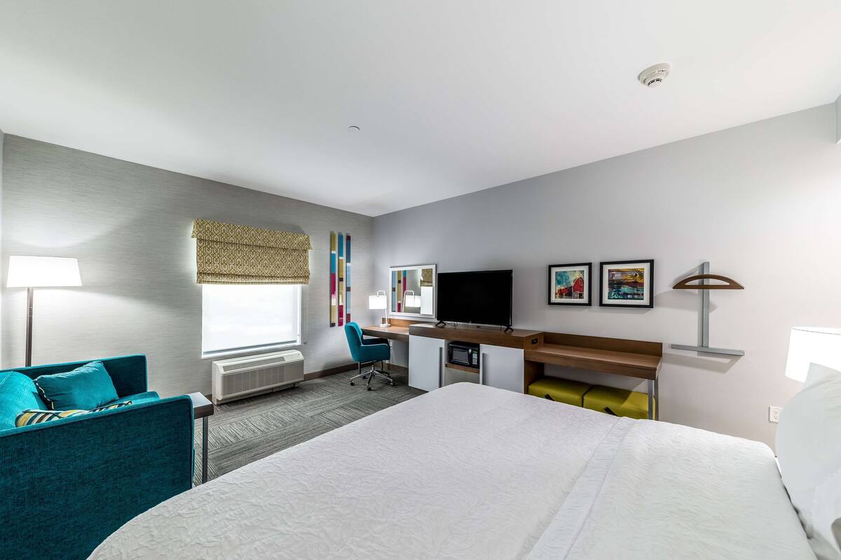 A hotel room with a bed, a desk with a computer, a TV, and a chair.
